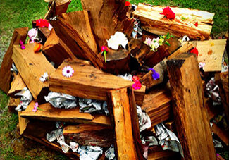 Wood ready to be lit into a fire. Small offerings of flowers and notes are scattered atop the wood.